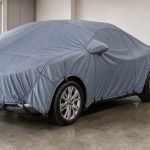 Voiture moderne argentée recouverte d’une bâche de protection ajustée dans un garage propre.
